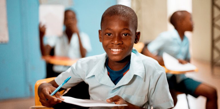 Young student smiling in classroom with peers, supporting education initiatives.